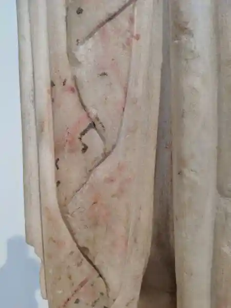 Detail of a marble kore statuette showing traces of red and dark painted decoration on the folds of the clothing.
